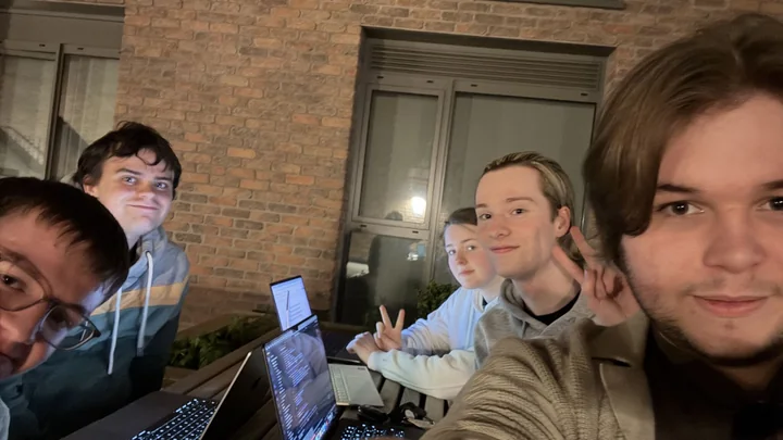 Five people taking a selfie around a table with open laptops
